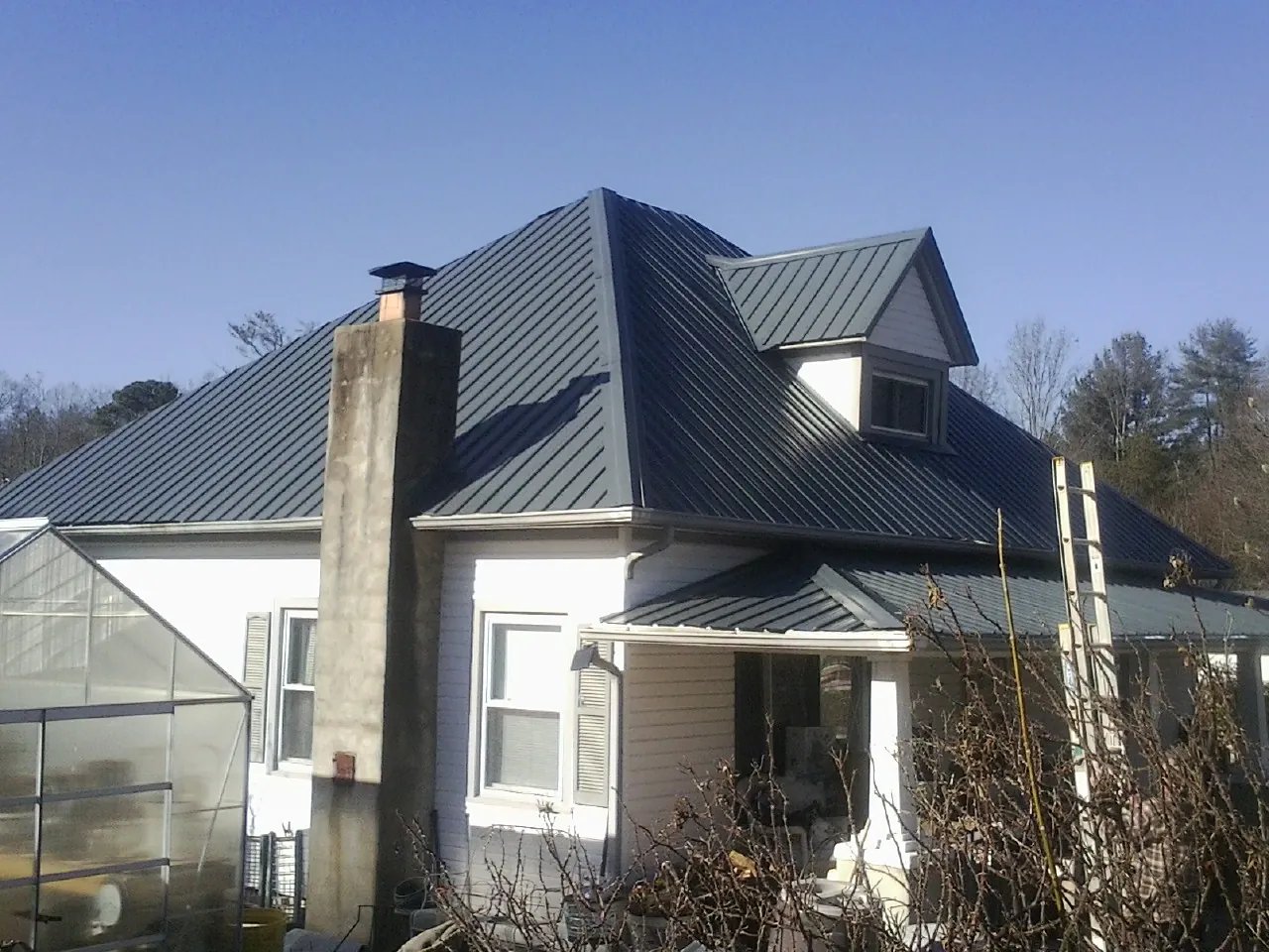 Dark blue standing seam metal roof on a white farmhouse with dormer — Slate & Tile Roof Repair by Roofing Brothers in Waubun