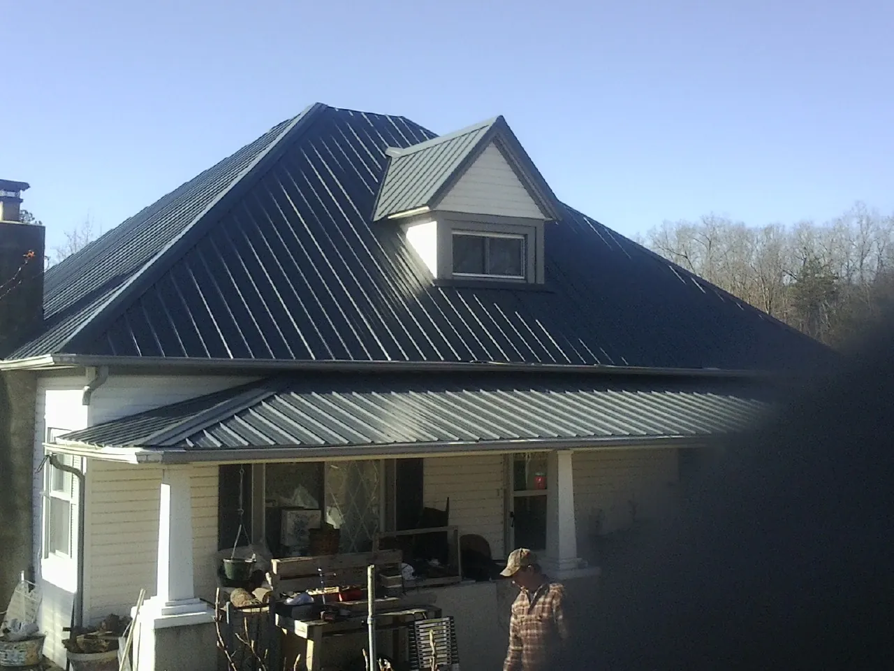 Dark blue standing seam metal roof with a dormer above a front porch in Waubun