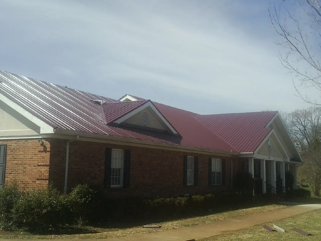 Red metal roof with gabled entries on a long brick building, from a Hail Damage Roof Repair job in Waubun