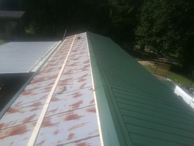 Old rusted panels beside newly installed green metal roofing — Wind Damage Roof Repair by Roofing Brothers in Waubun