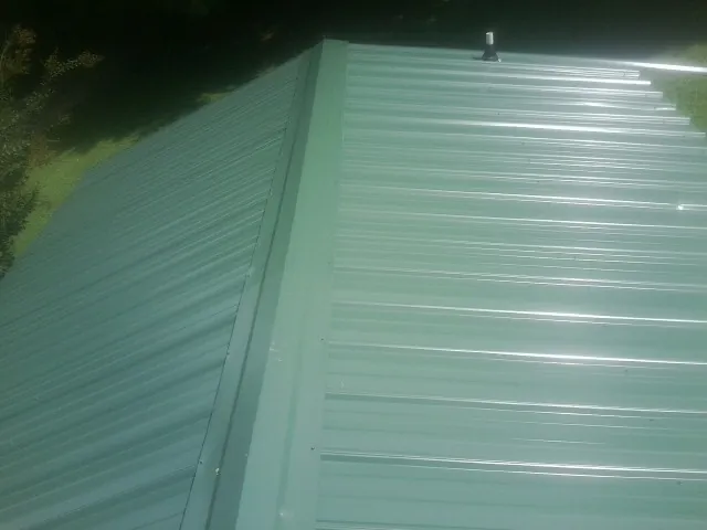 New green metal panels meeting at the ridge of a roof — Flat Roof Repair work by our crew in Waubun