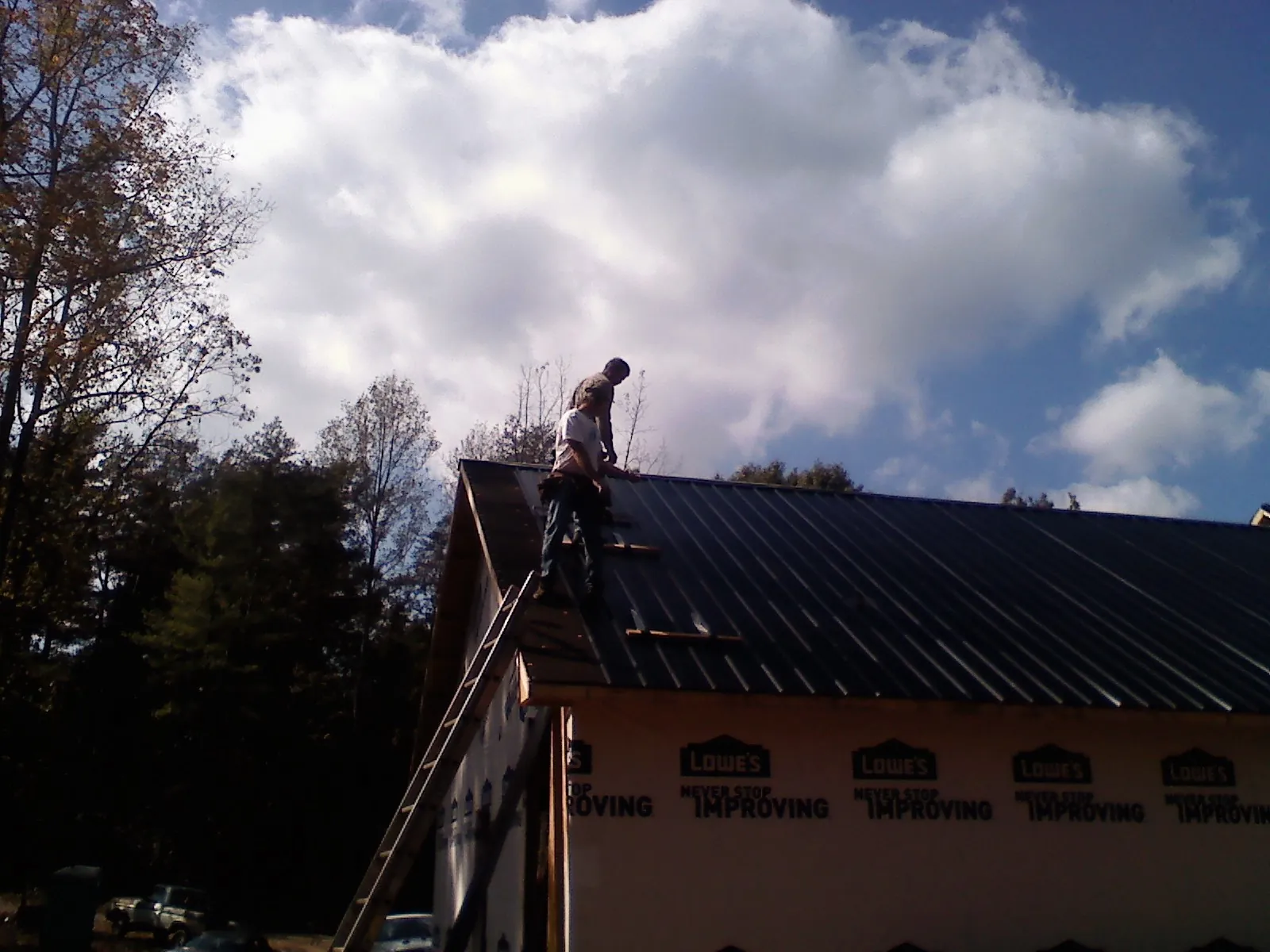 Roofer fastening dark metal panels high against a cloudy sky, from a Roof Inspection job in Waubun