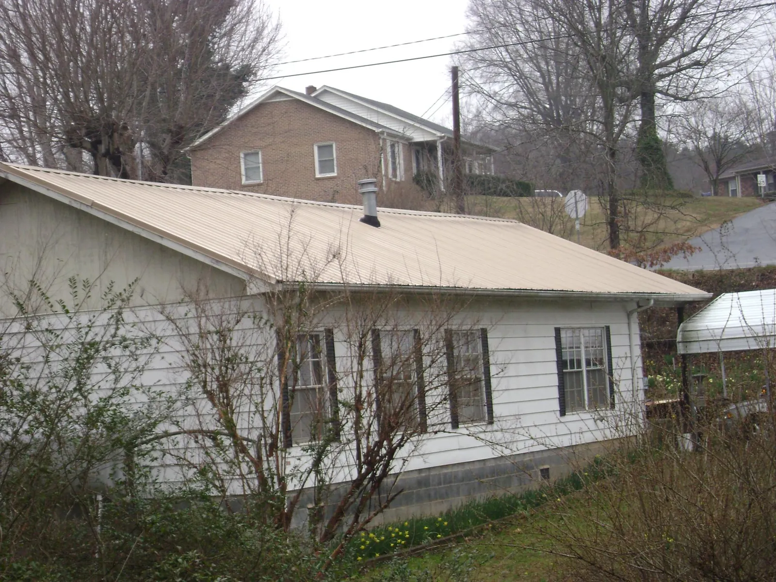 Tan metal roof on a white sided house set into a hillside — Commercial Roofing by Roofing Brothers in Waubun
