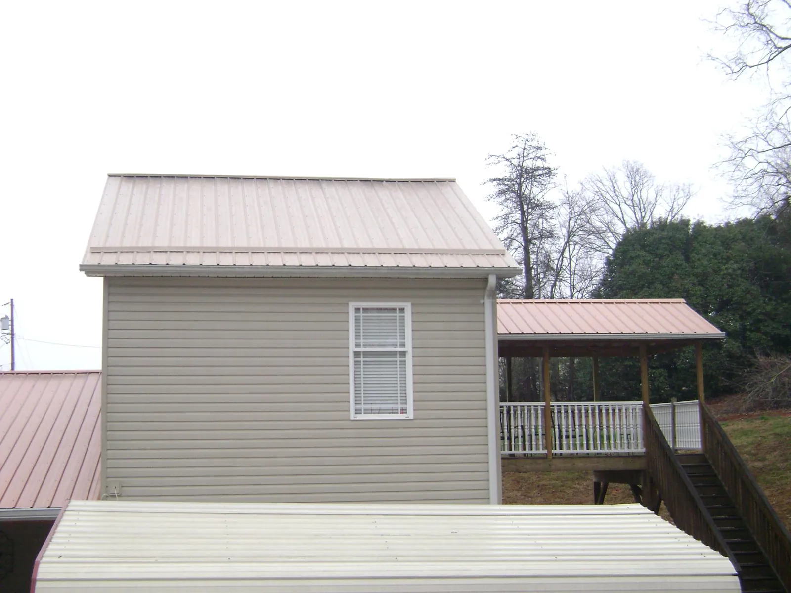 Tan metal roofs on a two story addition and attached porch, from a Roof Replacement job in Waubun