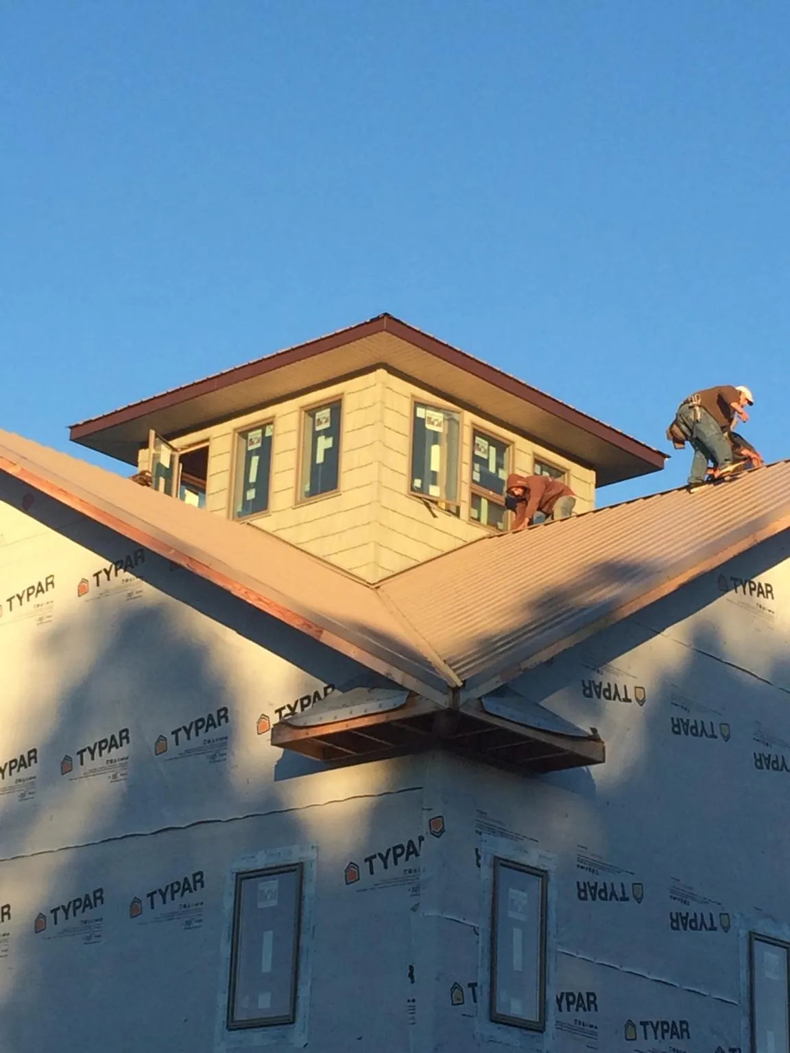 Roofers working around a rooftop cupola on a new metal roof at sunset — Roof Waterproofing in Waubun by Roofing Brothers